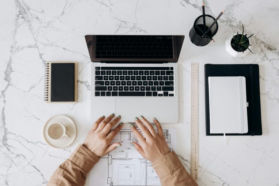 person in brown long sleeve shirt using macbook pro beside white ceramic mug